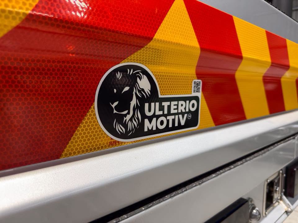 Reflective red-and-yellow chevron markings on a vehicle with a round ULTERIO MOTIV logo featuring a lion.