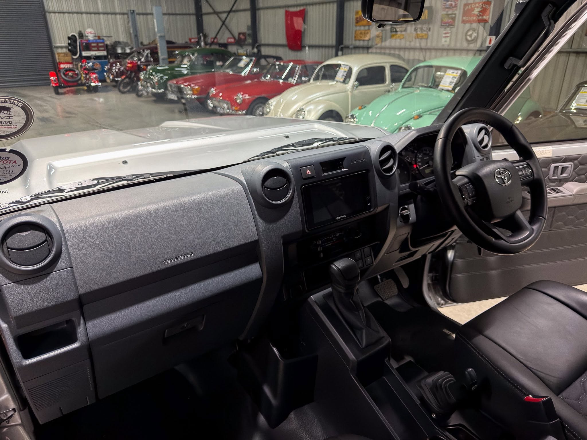 Right-hand-drive vehicle interior with steering wheel and dashboard, view of a vintage car showroom through the windshield