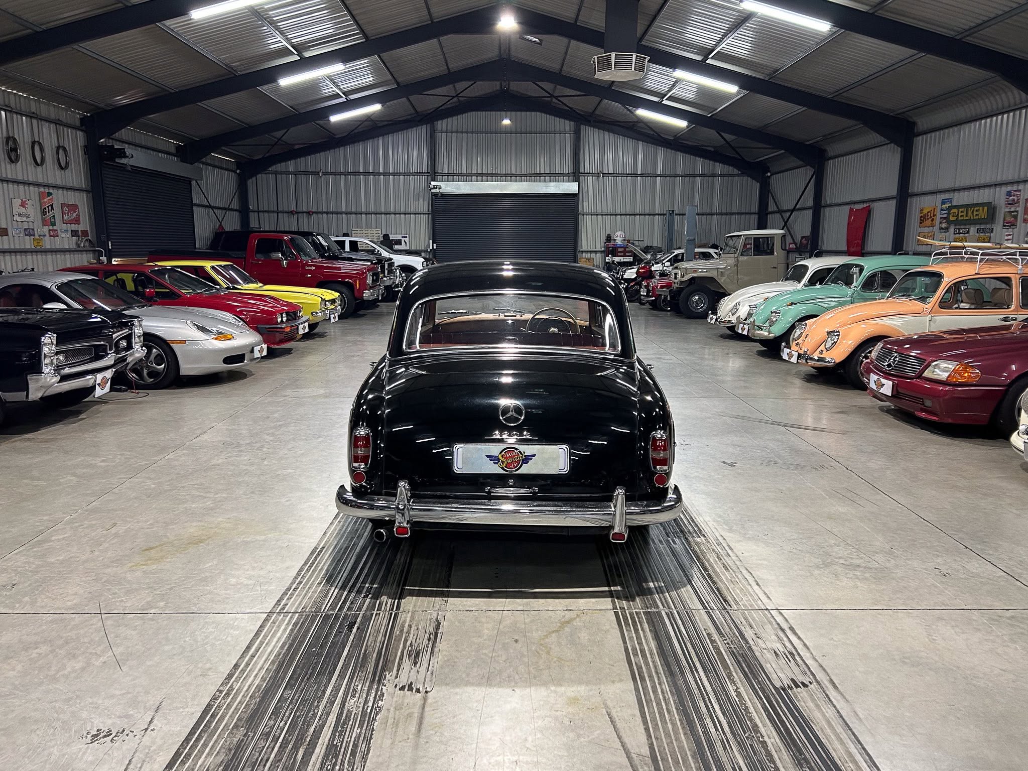 Interior of a large metal showroom filled with rows of classic cars on both sides, a black vintage car centered in the foreground.