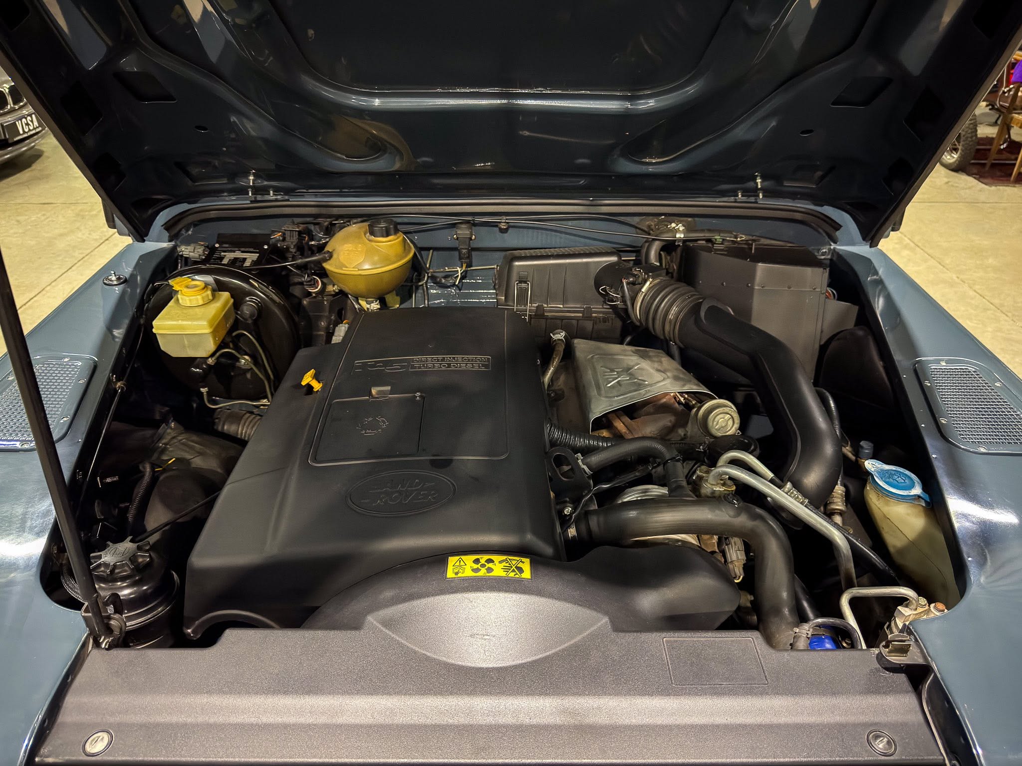 Open car hood showing the diesel engine bay with a yellow coolant reservoir and air intake hoses.