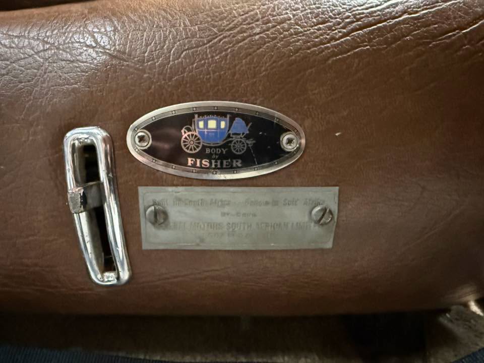 Vintage car interior detail: Fisher Body emblem on brown leather with a chrome latch and metal nameplate plate nearby.