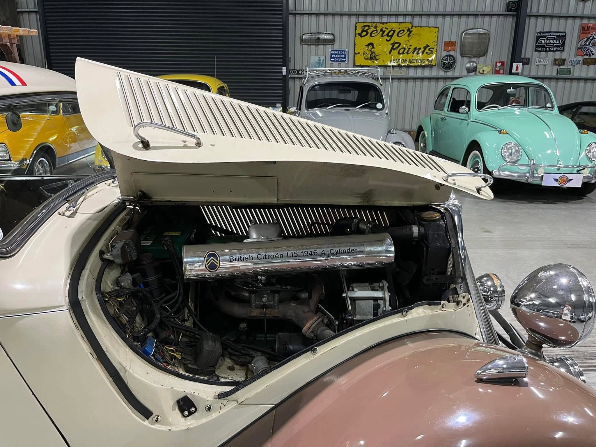 Open hood of a white vintage car revealing its engine, with other classic cars in a retro showroom.