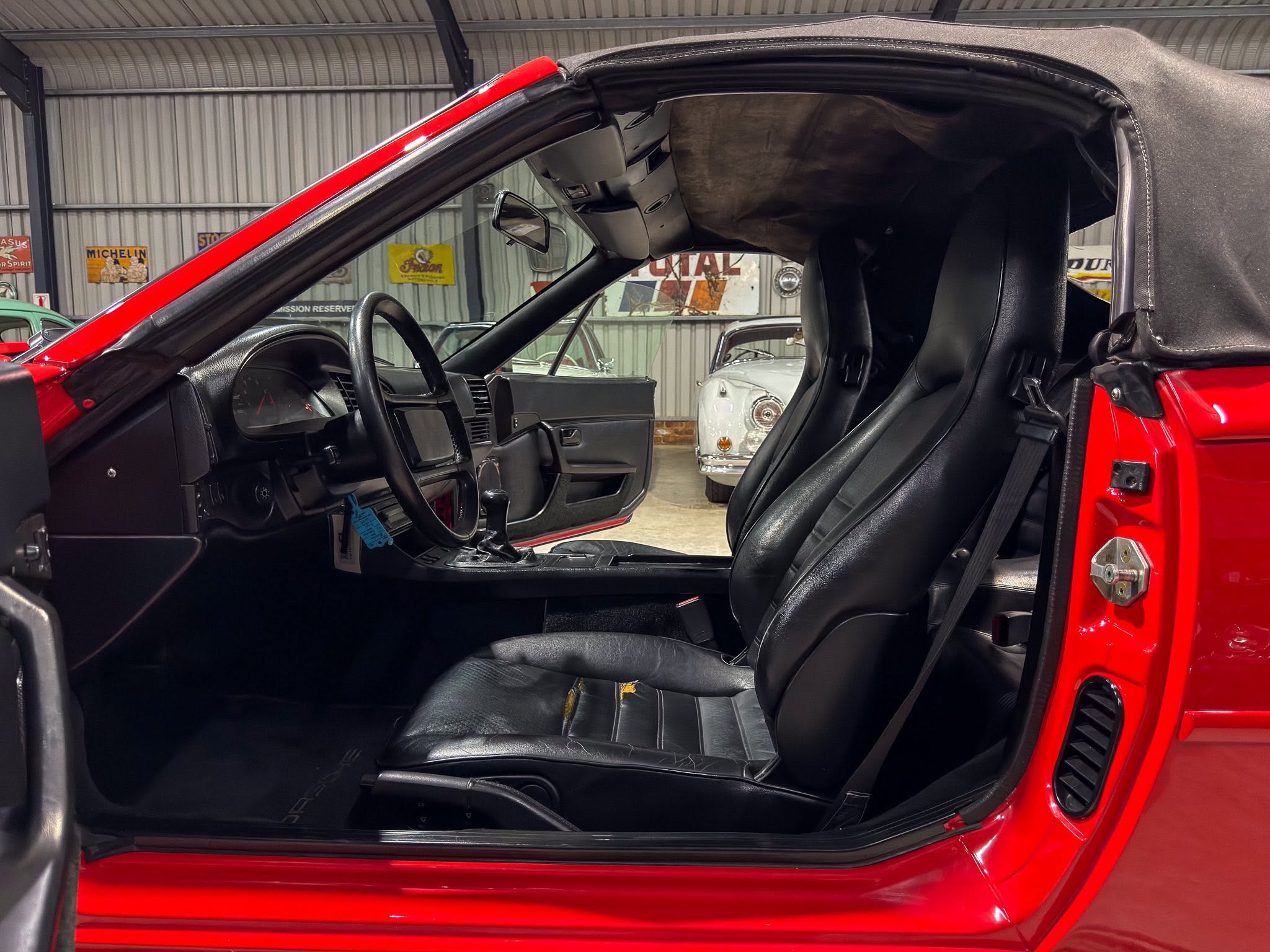 Red convertible interior with black leather seats and the roof folded back, in a showroom setting