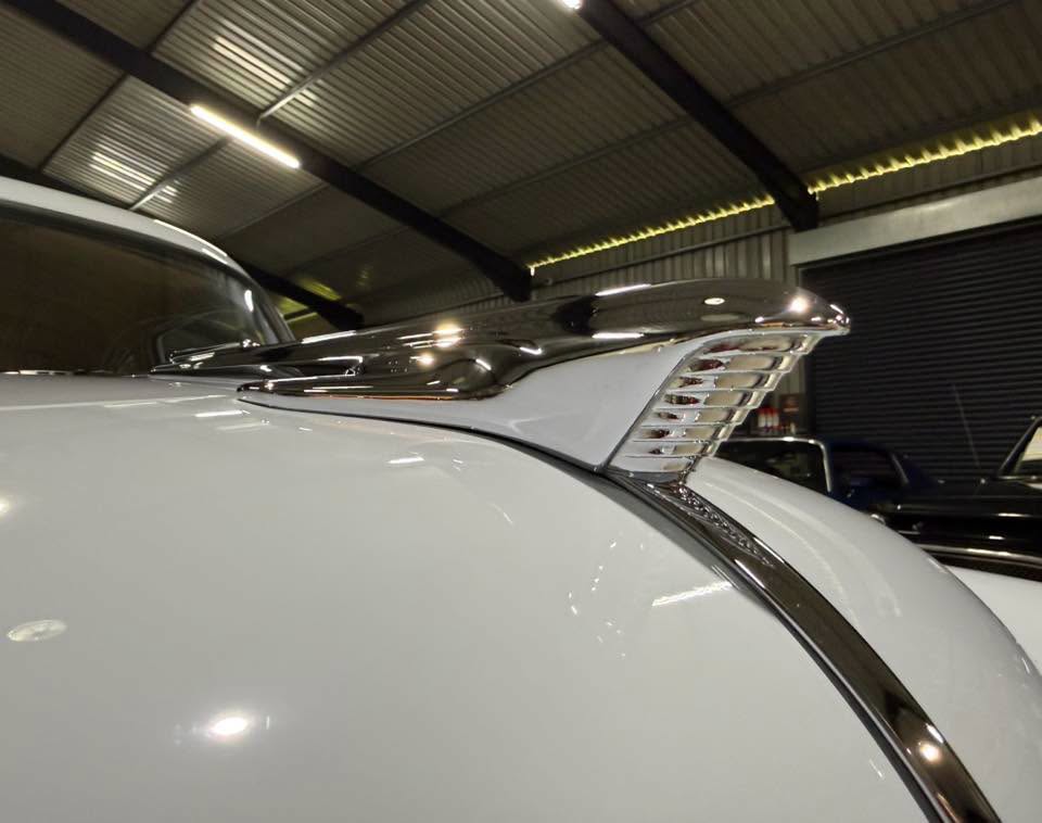 Chrome hood ornament on a white vintage car, indoors in a showroom or garage setting
