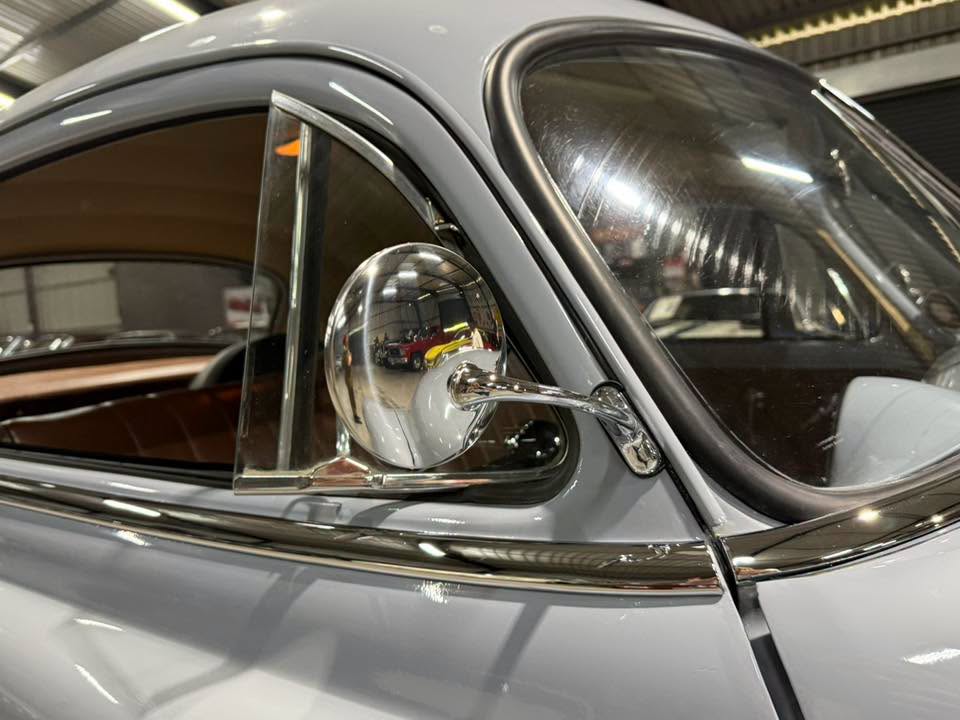 Close-up of a vintage car's chrome side mirror and window trim on a light blue body, brown interior visible inside the car.
