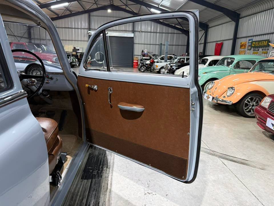 Open car door in a vintage showroom, showing brown door panel and interior seating.