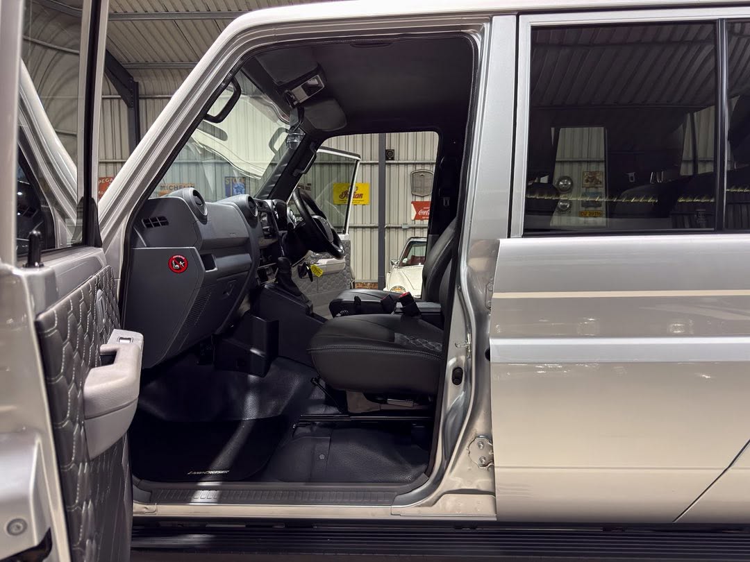 Open driver’s-side door reveals the front cabin of a silver pickup/SUV, showing the gray dashboard, steering wheel, and black seat in a workshop setting