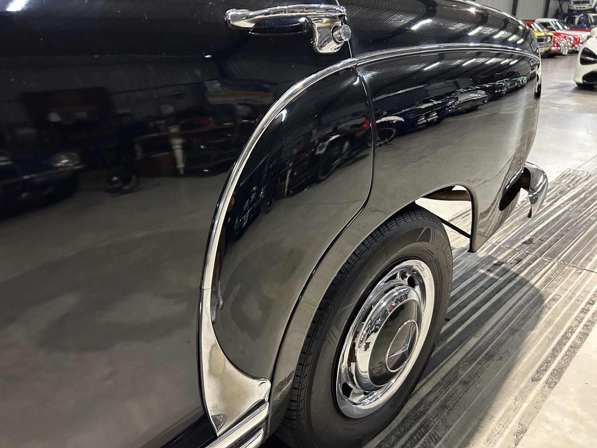 Close-up of a black vintage car's rear quarter panel with chrome trim and wheel in a showroom.