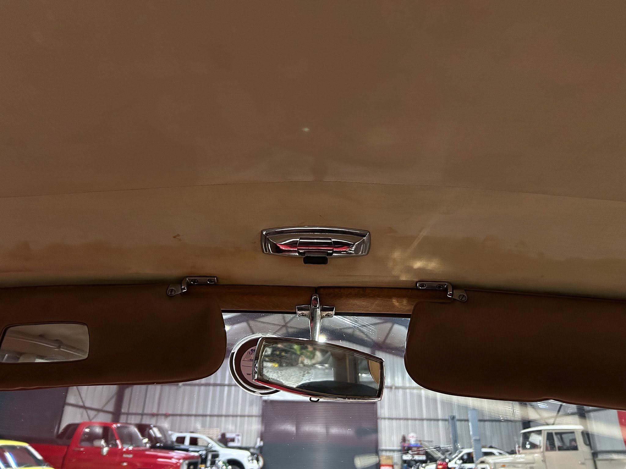 Beige car interior viewed from the back seats, showing the ceiling and overhead handles; showroom with cars outside through the windshield