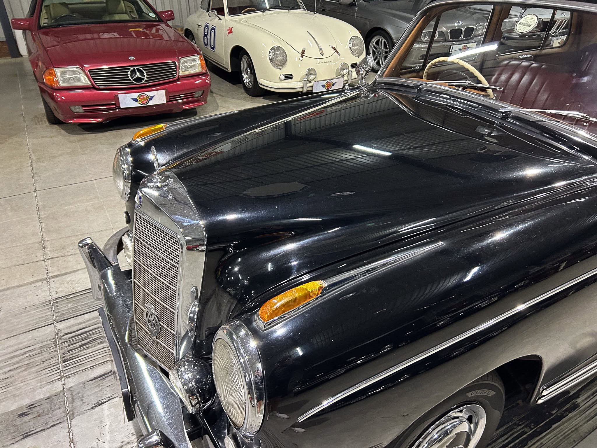 Close-up of a black vintage car's front with chrome grille and round headlights in a showroom, other classic cars visible in the background.