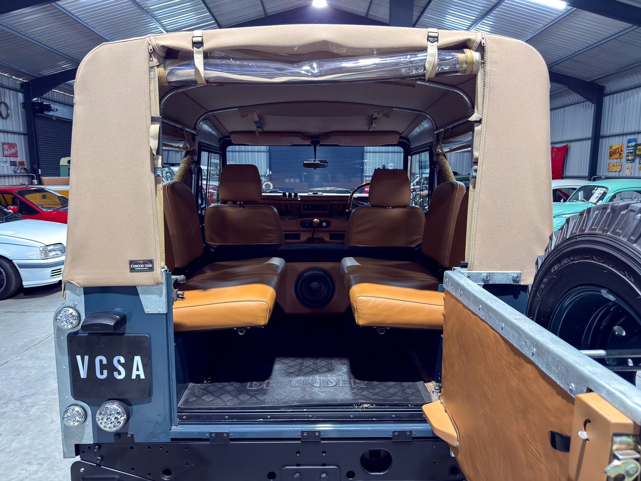 Rear view of a vintage off-road vehicle with tan seats and a soft top folded open, inside cockpit visible and workshop background.