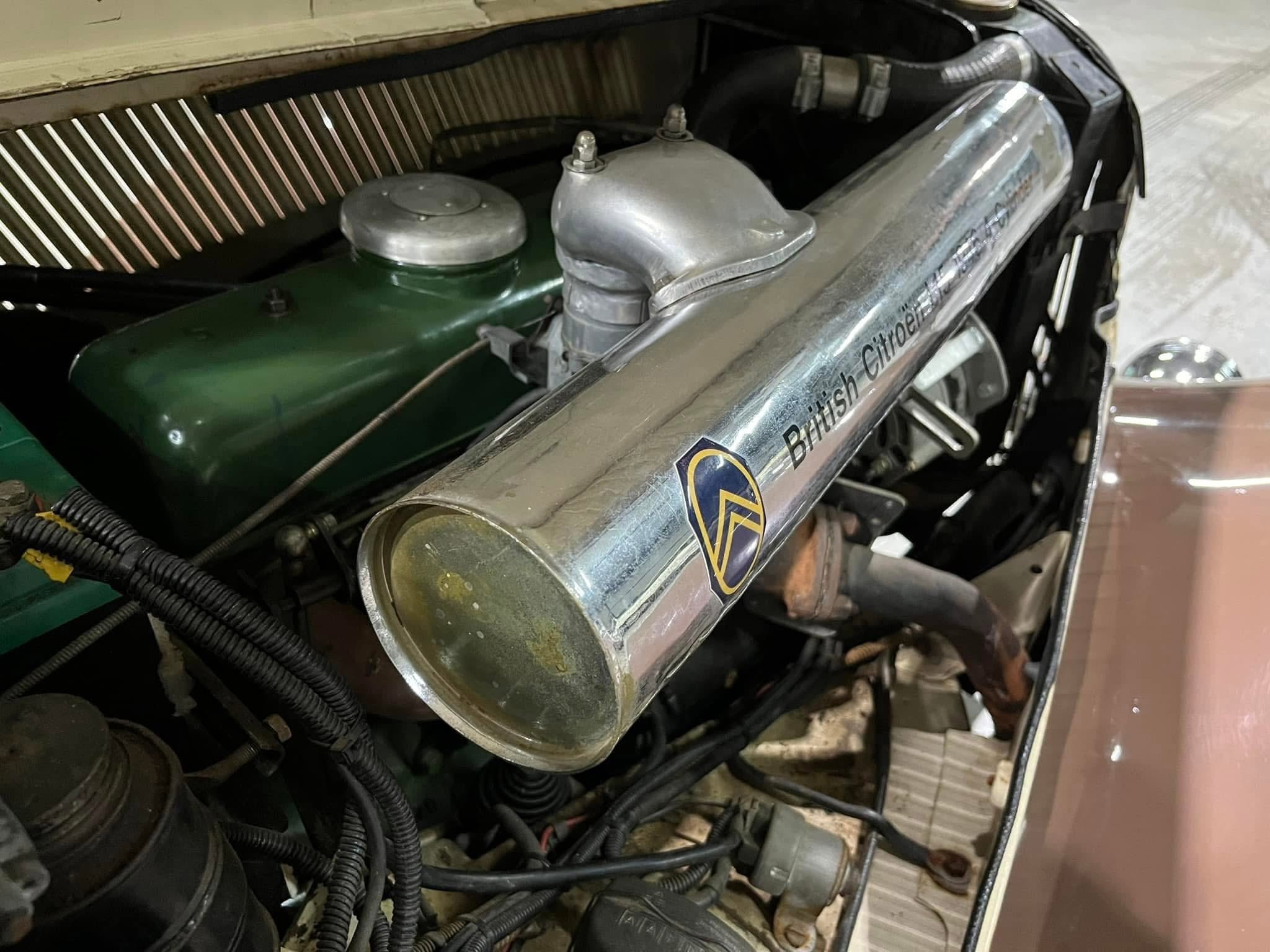 Close-up of an old car engine bay under the open hood, showing a chrome air filter housing and green engine block.