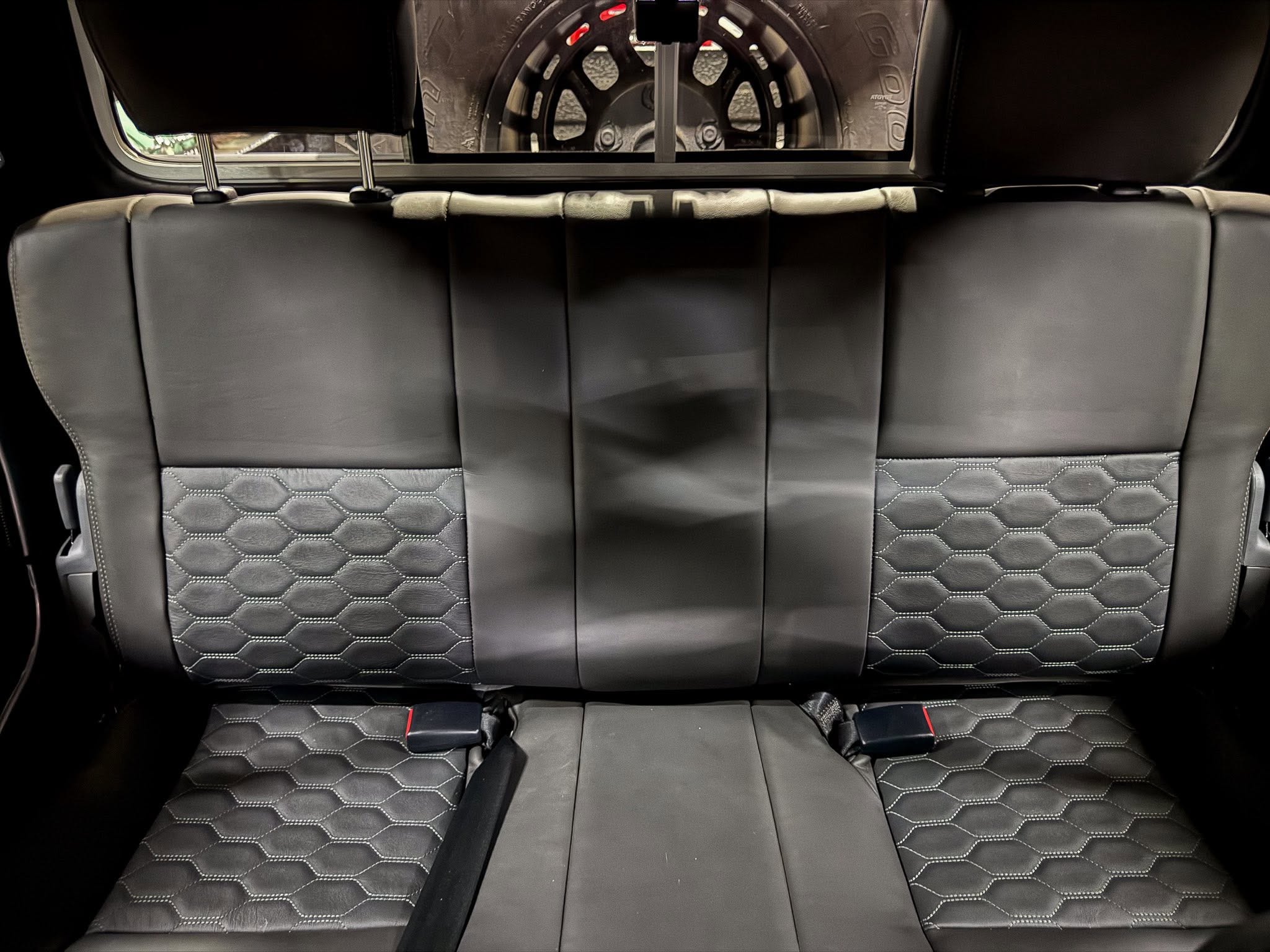 Rear car seats in black leather with hexagonal stitching and visible safety belts.