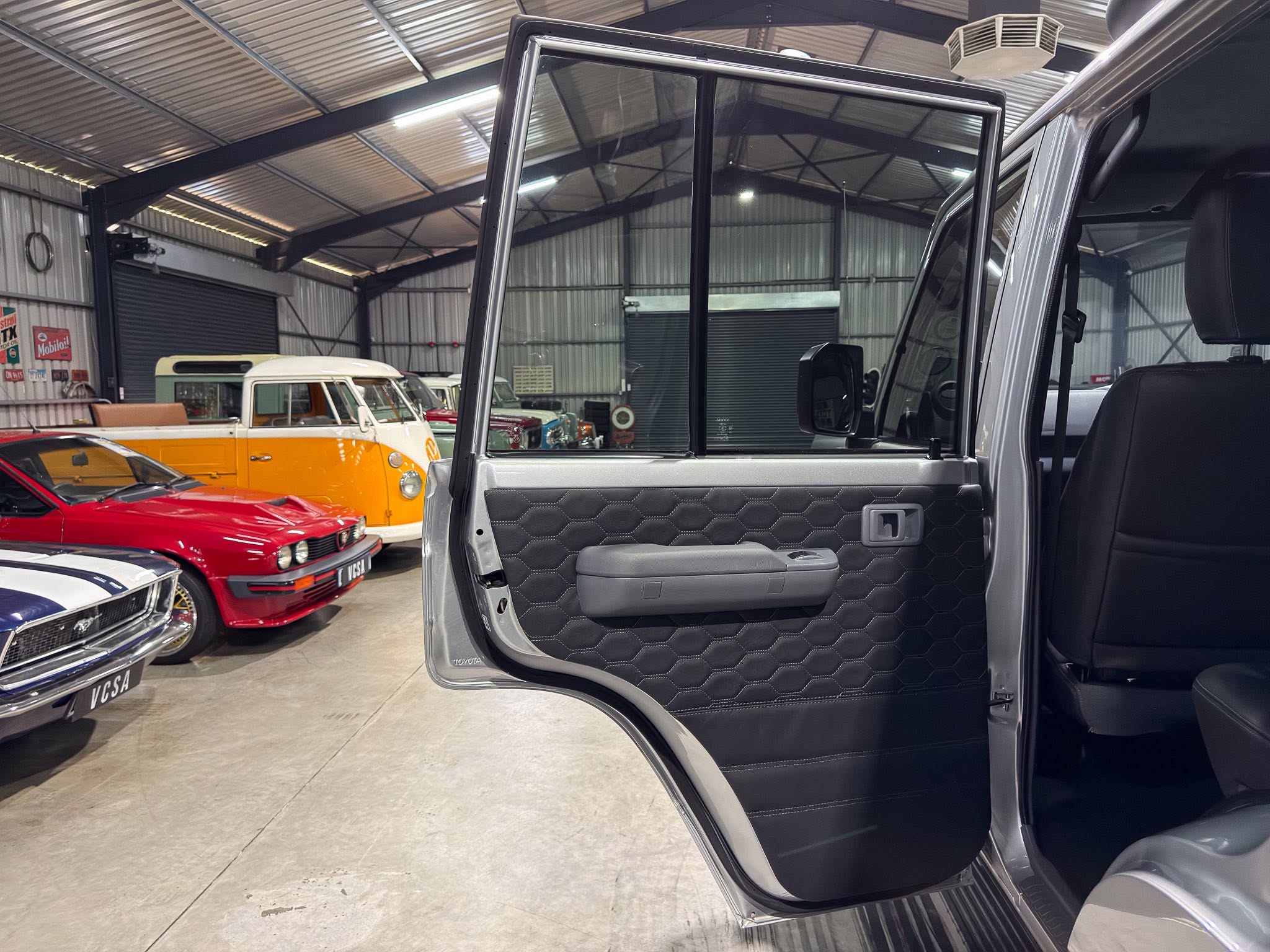 Open car door in a metallic SUV inside a vintage car showroom with classic cars parked in a warehouse.