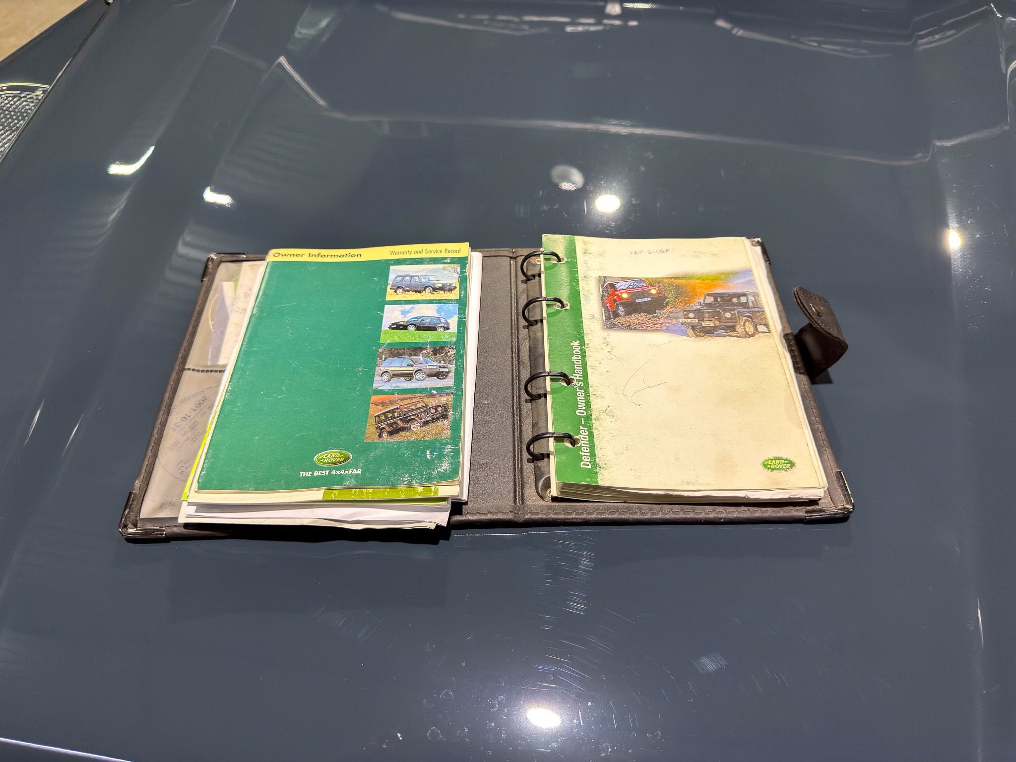 Open binder with green Land Rover vehicle manuals spread on a dark blue car hood.