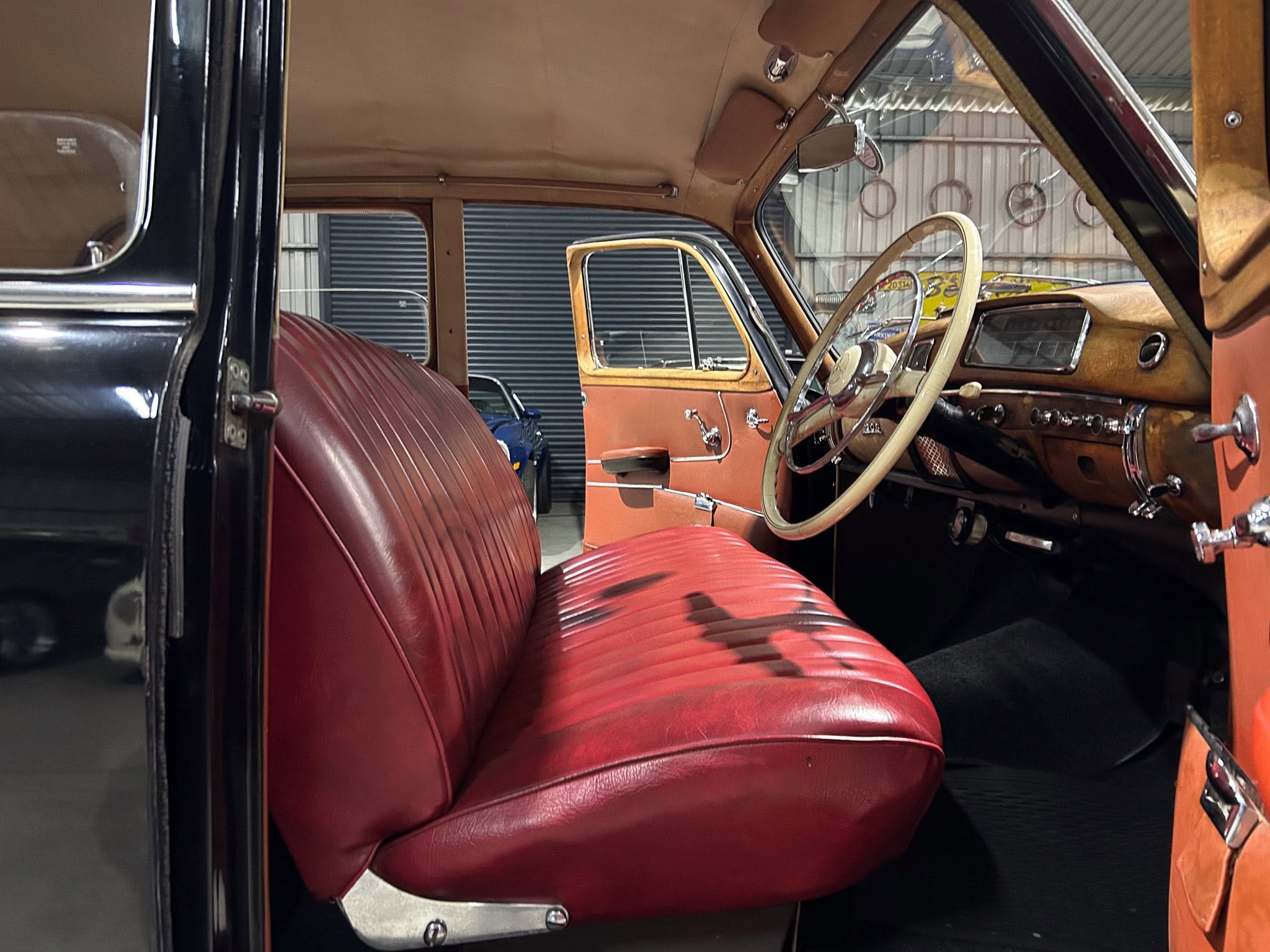 Interior of a vintage car with red leather seats, tan headliner, and wooden dashboard trim visible by the steering wheel.