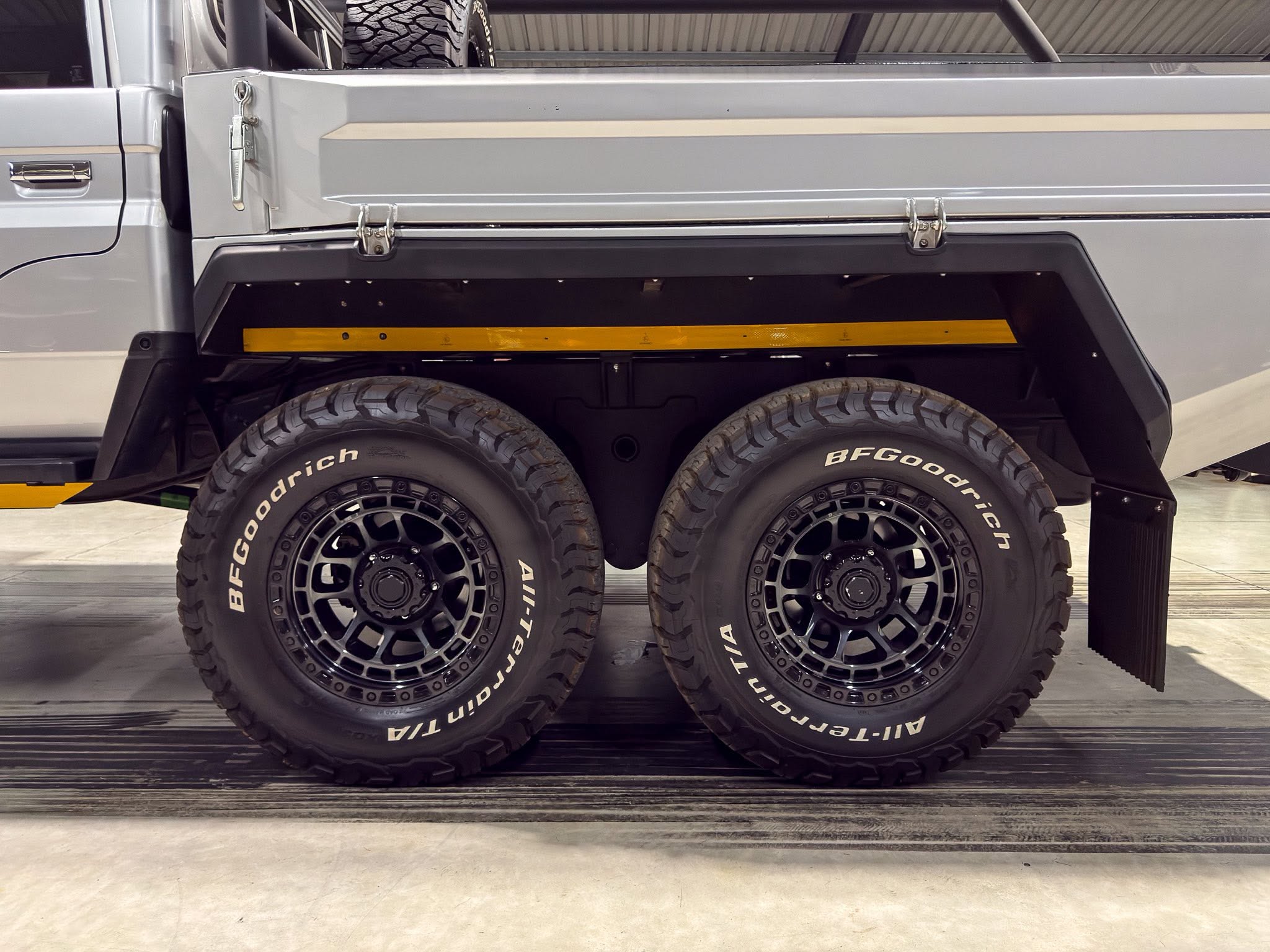 Close-up of a heavy truck’s dual rear wheels and metal cargo bed with a yellow reflective strip above the tires.