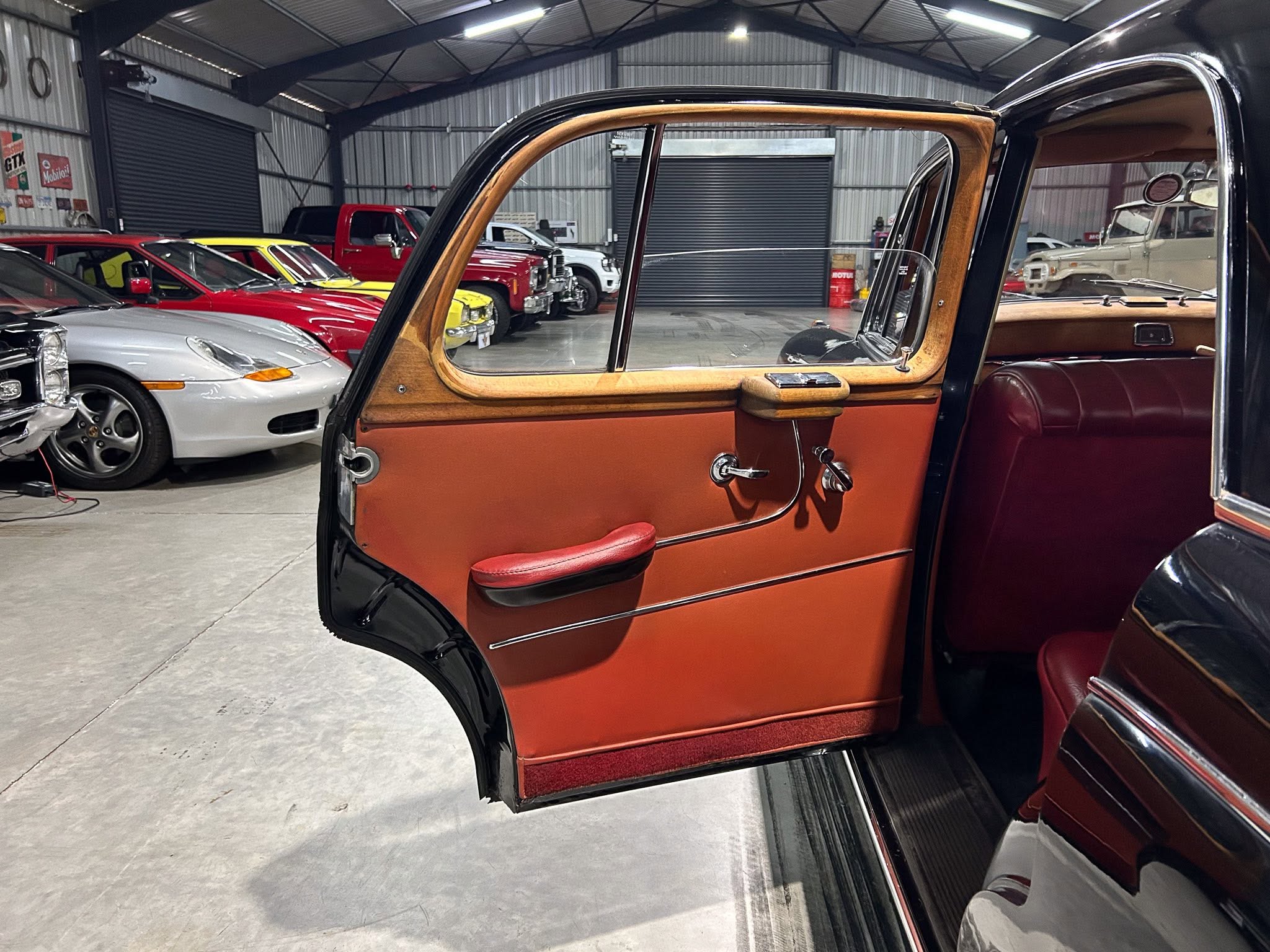 Open door of a vintage two-tone brown and tan car interior with wood trim around the window, in a showroom filled with classic vehicles.