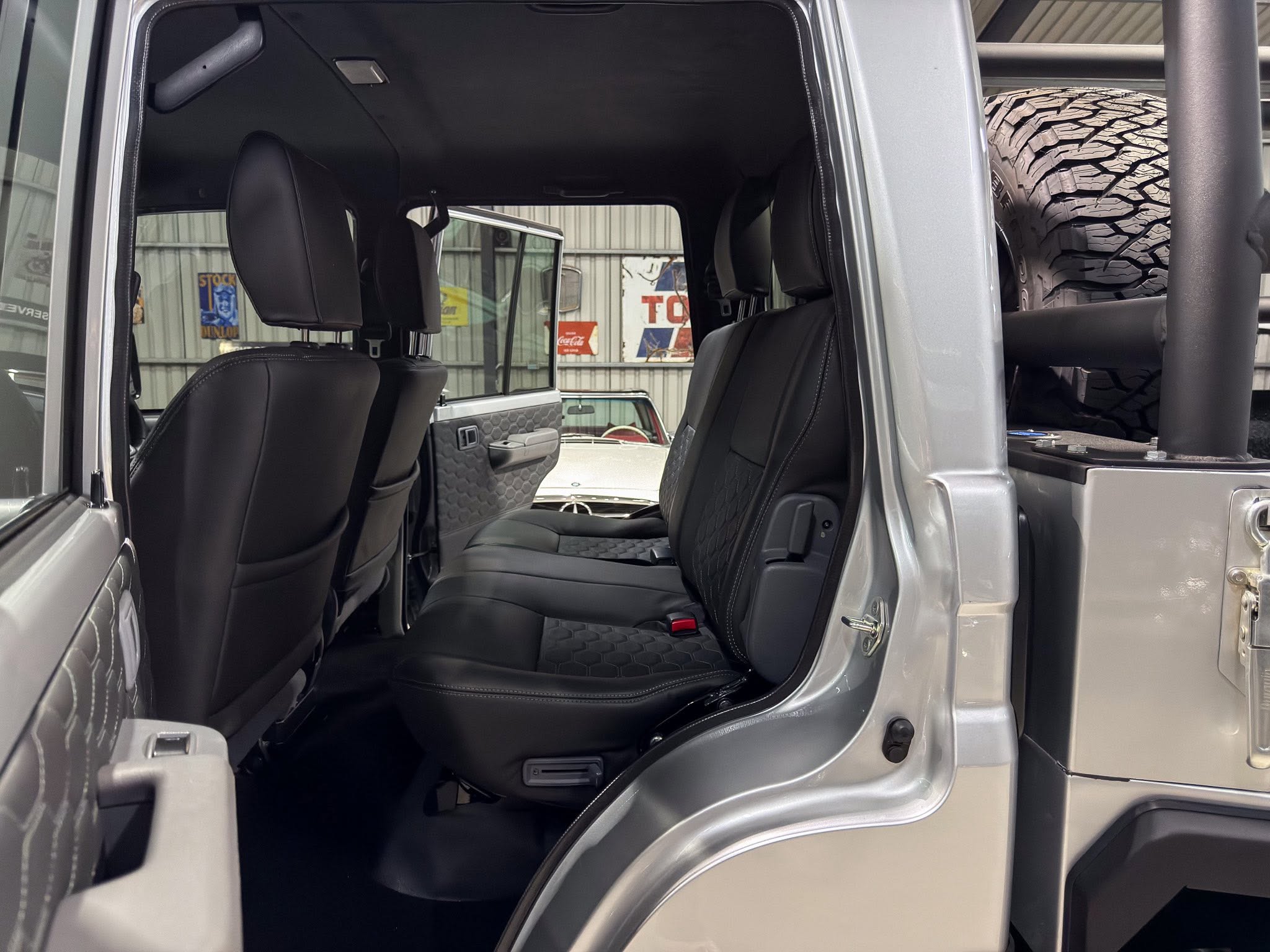 Interior of a gray SUV with black leather seats, rear doors open and a large off‑road tire visible on the outside (right).