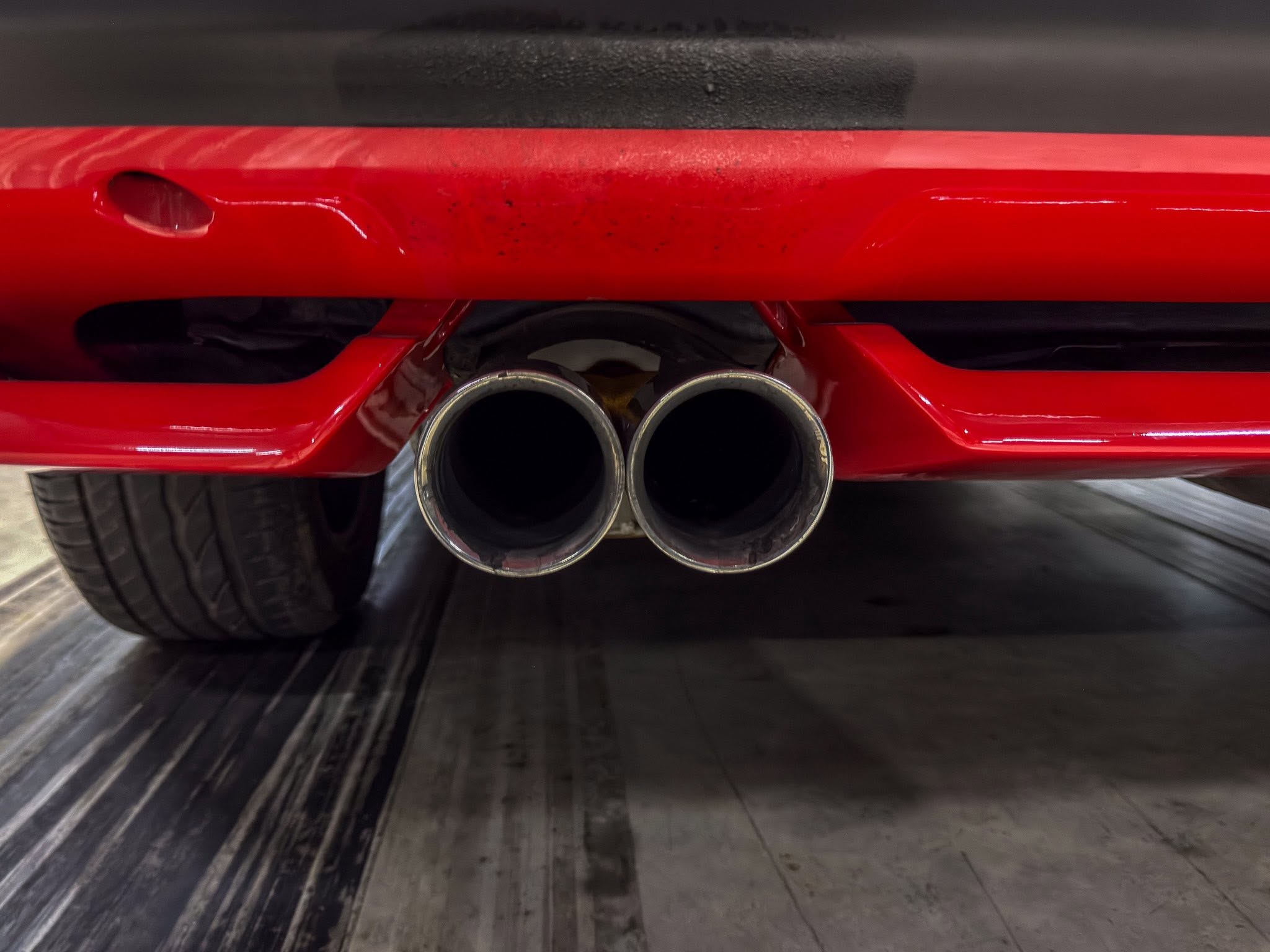 Rear view of a red car showing twin chrome exhaust tips beneath the bumper in a garage.