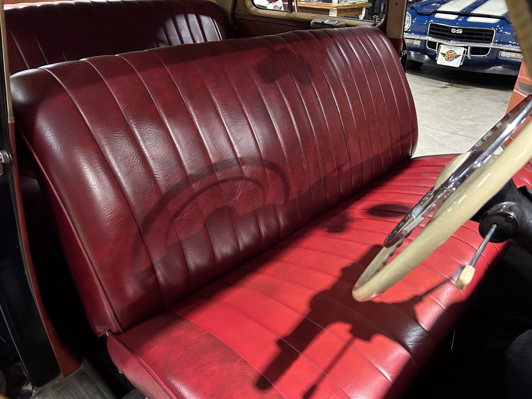 Red leather car bench seat from a vintage automobile, with a beige steering wheel and chrome trim nearby.