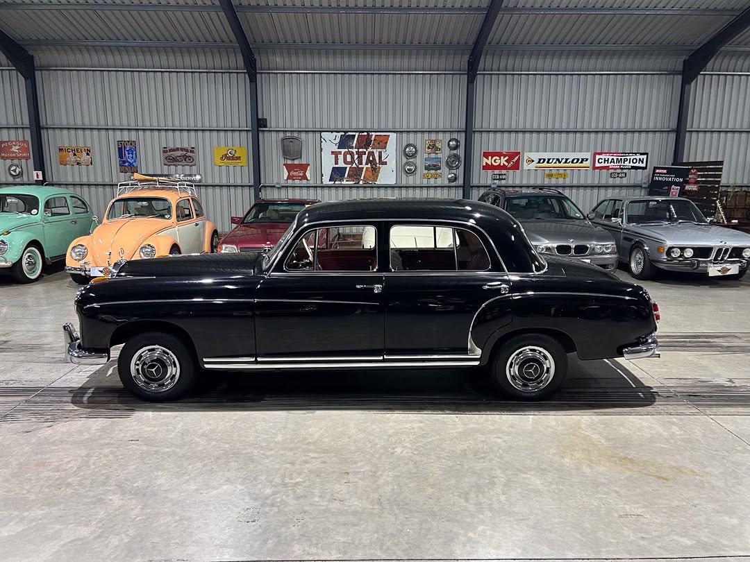 Side view of a black vintage sedan with chrome trim inside a classic car showroom, with other antique cars in the background.