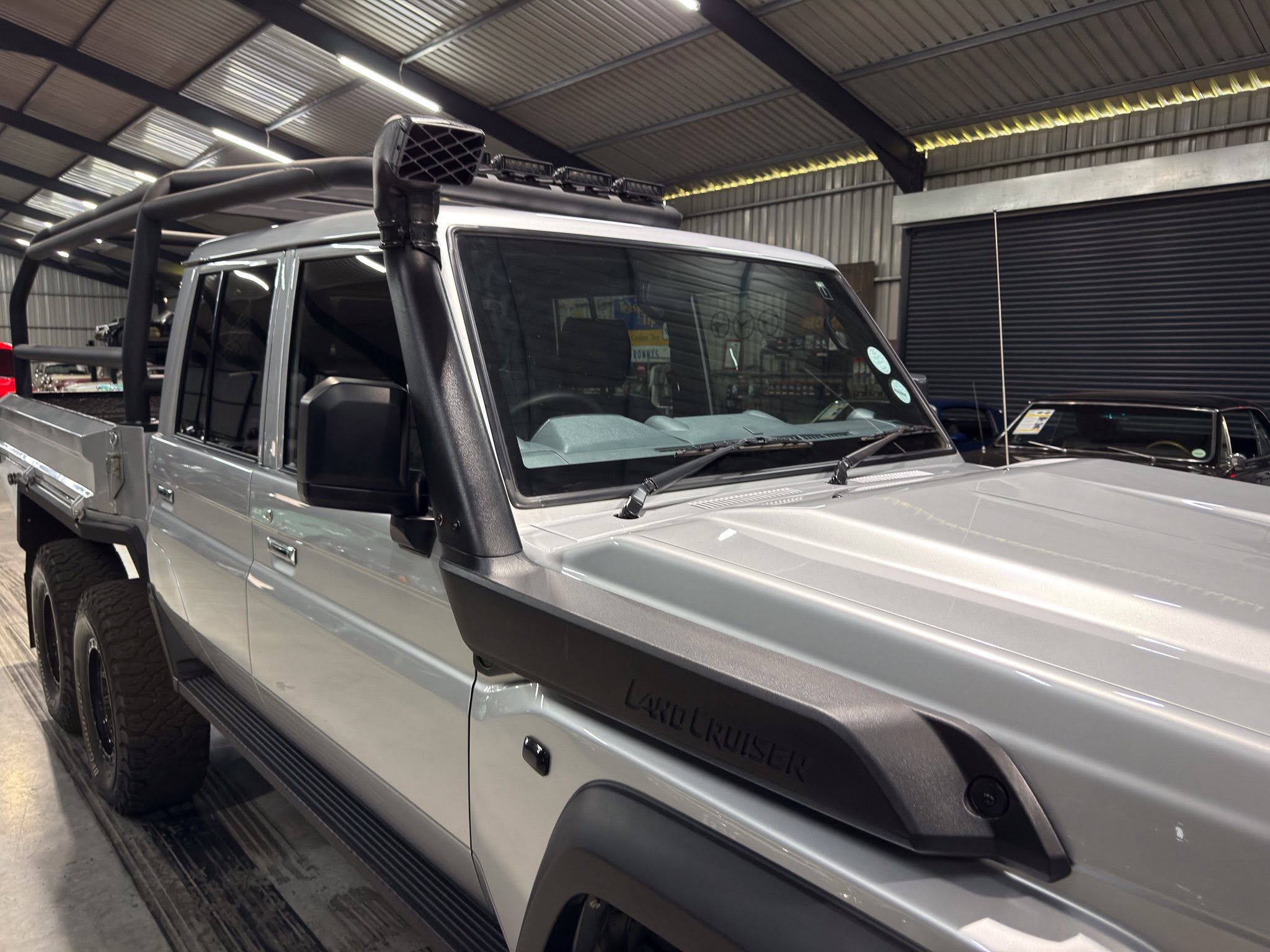 Silver Mercedes-Benz G-Class pickup in a garage with roof rack and auxiliary lights on top, showing rugged off-road styling.