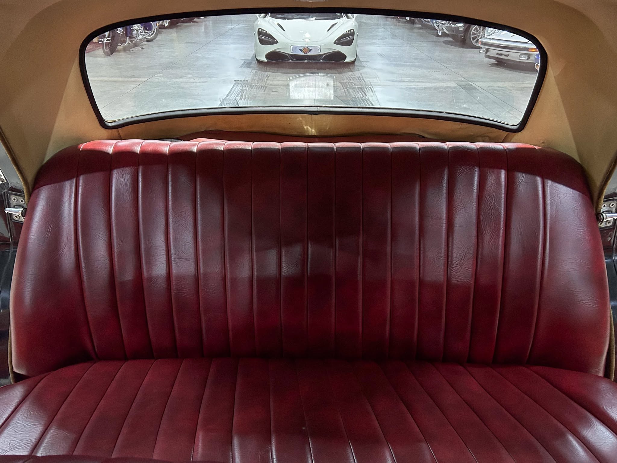 Backseat view of a car with red leather upholstery; a white sports car is visible through the rear window in a showroom.