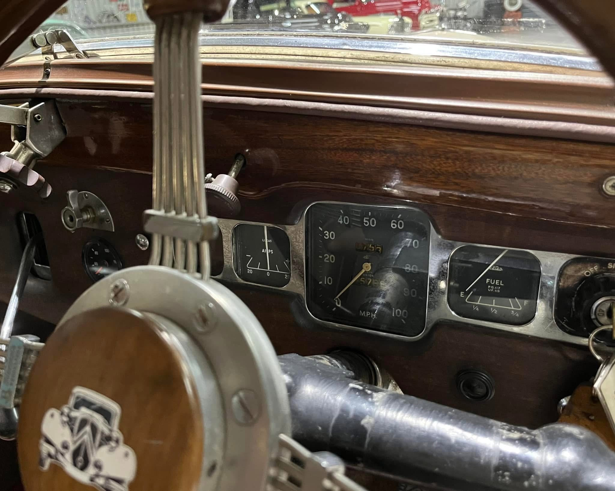 Interior of a vintage car showing wood paneling, old-style gauges, and a large steering wheel near the pedals