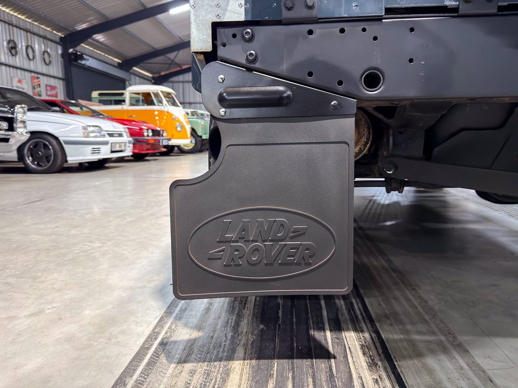 Close-up of a car lift with a Land Rover badge, in a workshop with vintage cars in the background.