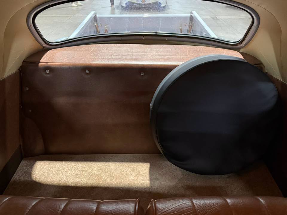 Interior of a vintage car trunk with brown leather panels and a large black spare tire cover on the right side.