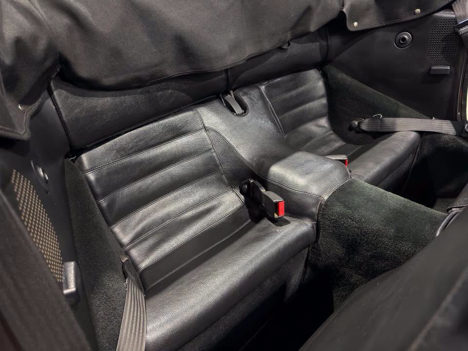 Black leather car rear seats with three seating positions and visible red seat belt buckles