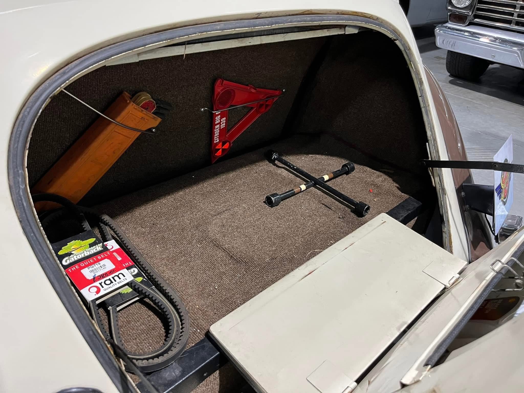 Open car trunk with a red scissor jack and a wooden tool box, plus belts and rods on brown carpeted floor