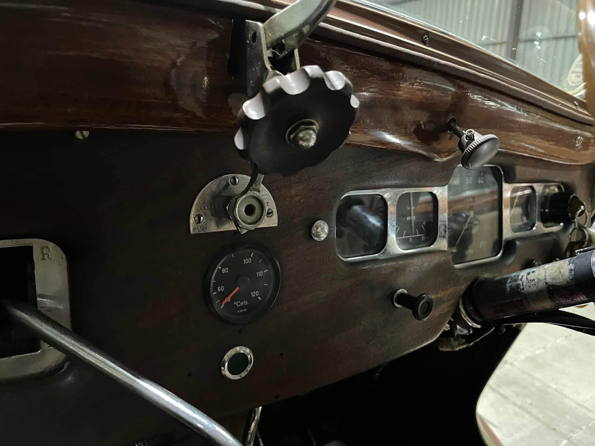 Close-up of a vintage car dashboard with dark wooden panel, metal knobs, and gauge cluster visible on the right arm of the photo.