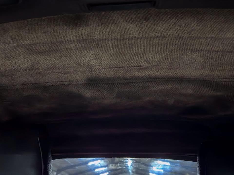 Dark vehicle interior view with fabric headliner and a curved window showing blue-lit tunnel outside.