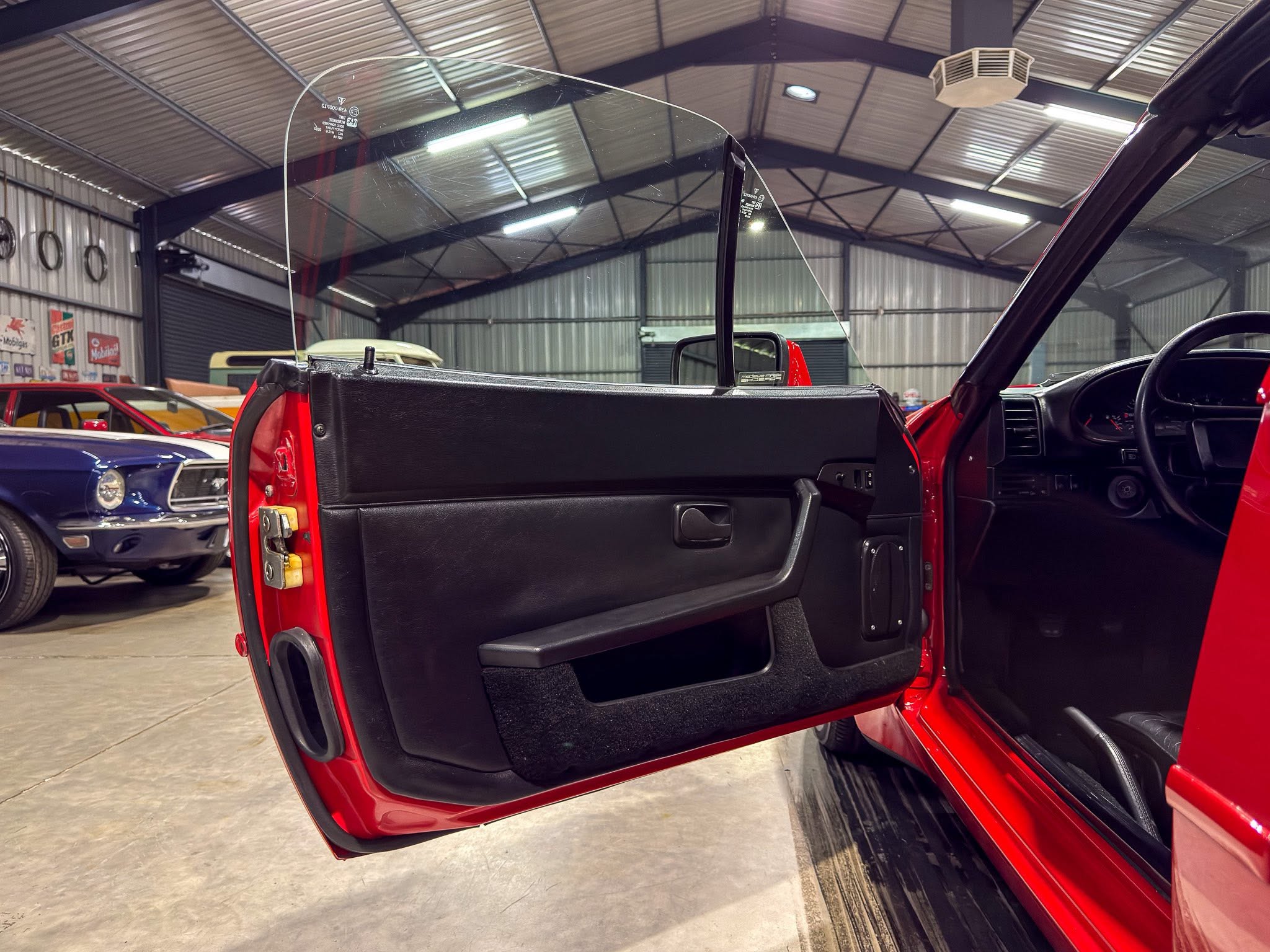 Open door of a red convertible in a large garage, with other classic cars visible in the background.