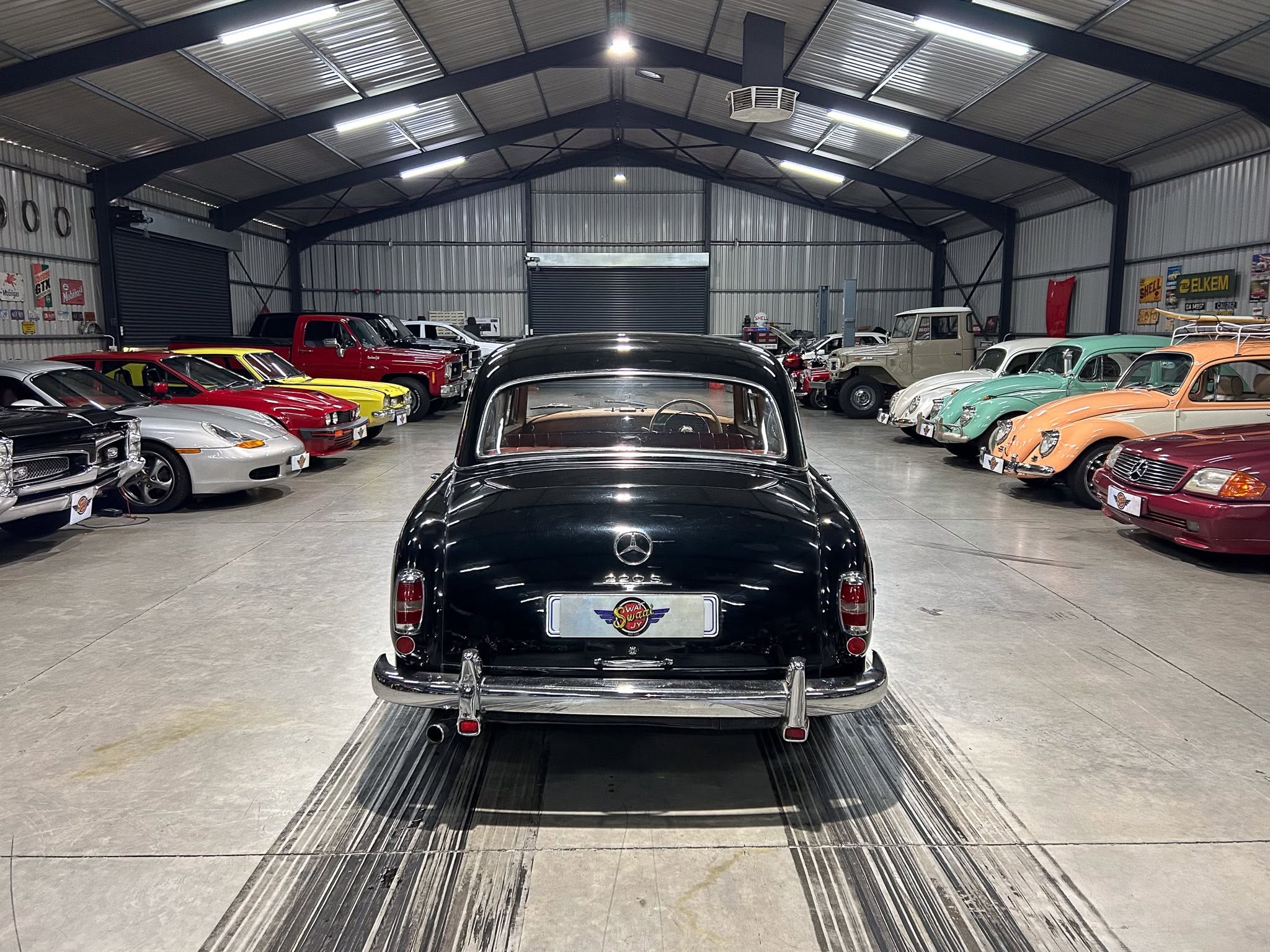 Indoor showroom filled with vintage cars lined up along both walls, black classic car in foreground.