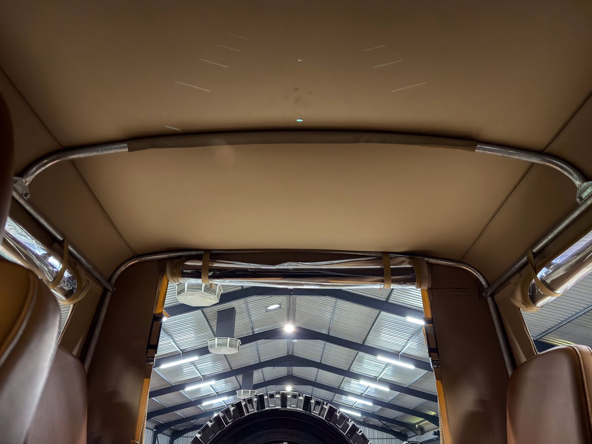 Inside a car's trunk seen from the rear, with a large spare tire laid flat and tan leather lining surrounding metal support rails above.