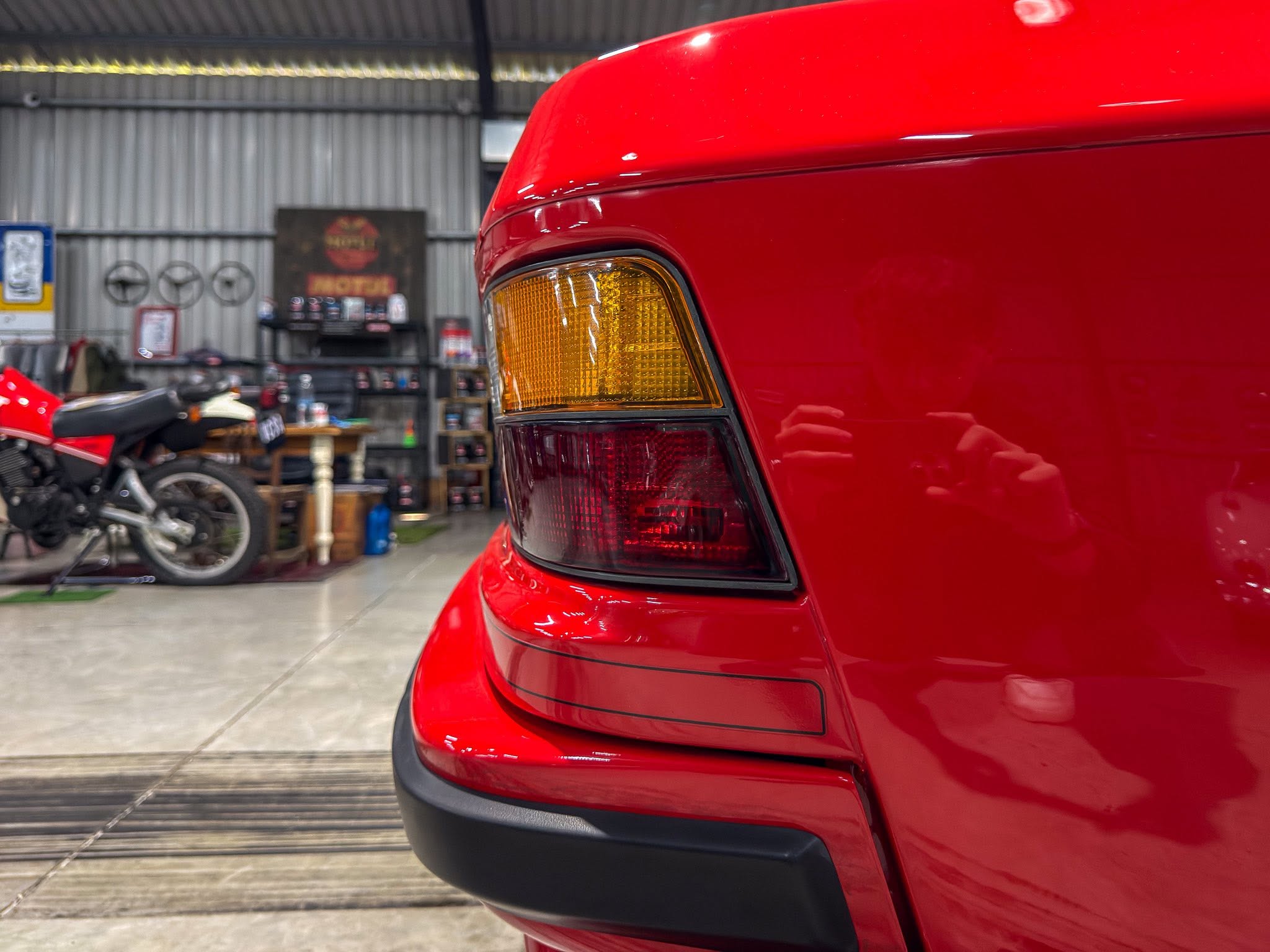 Close-up of the rear corner of a red car, displaying the amber turn signal in a workshop setting.