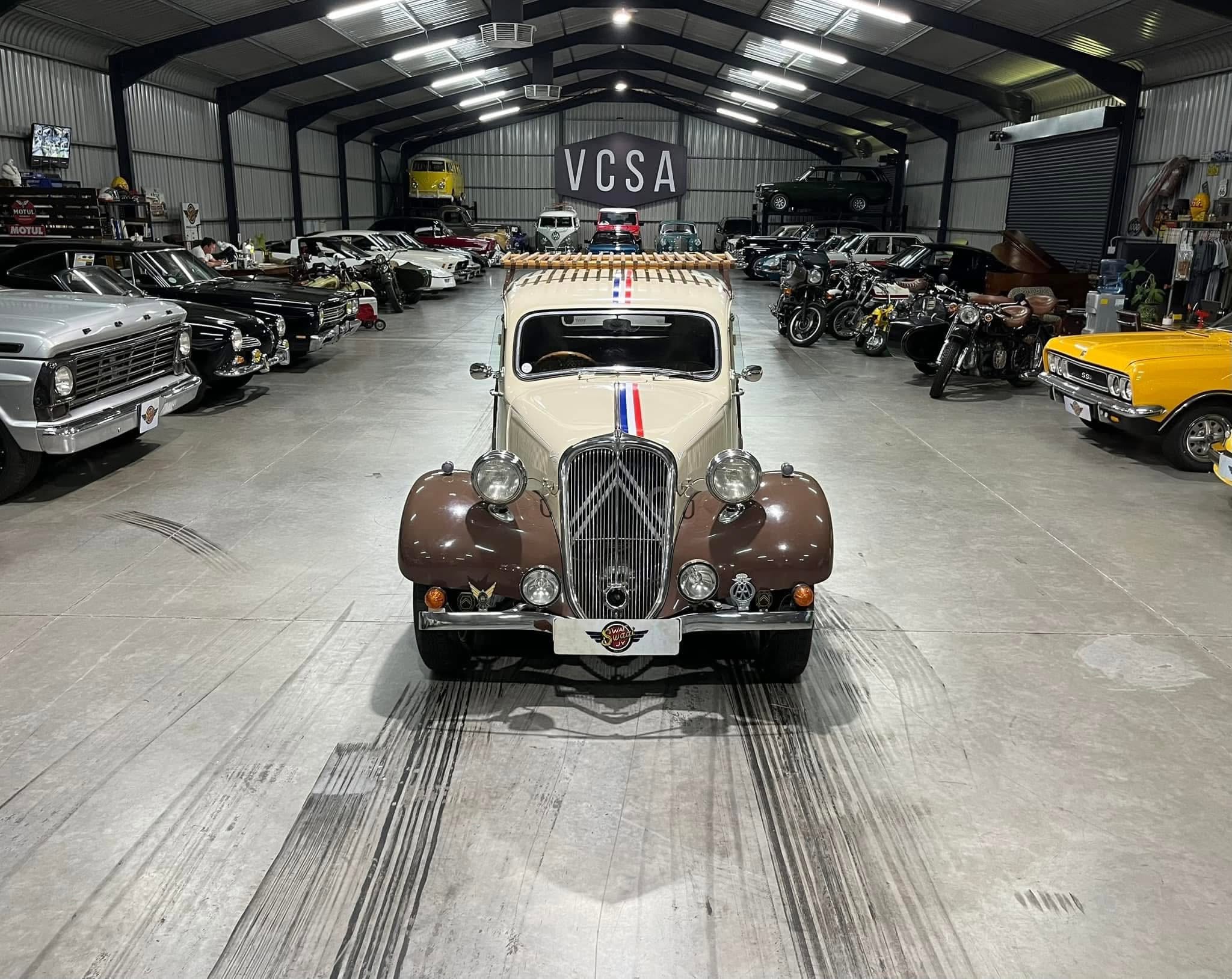 Indoor car showroom or museum filled with vintage vehicles, seen from a front-center view of a classic car with a red, white, and blue stripe.