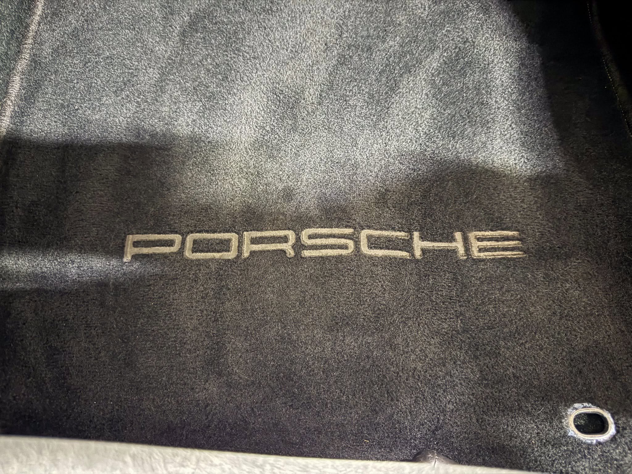 Porsche logo embroidered on a black textured car trunk mat edge visible on the right side