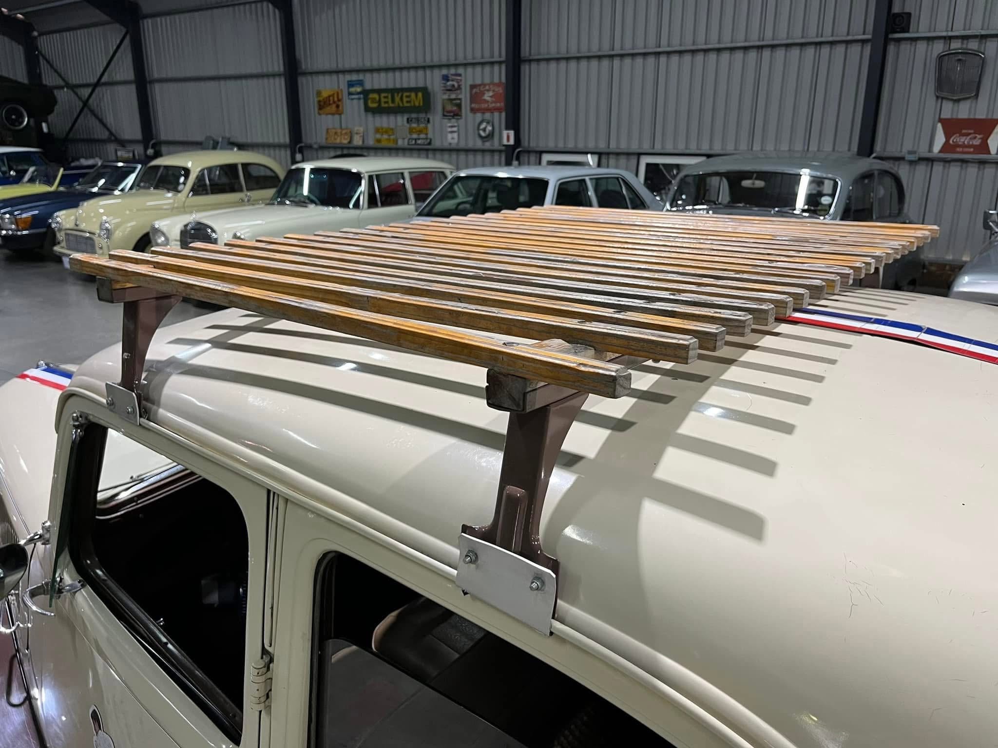 Indoor garage with several vintage cars parked in a row; a wooden roof rack sits across the white car in the foreground.