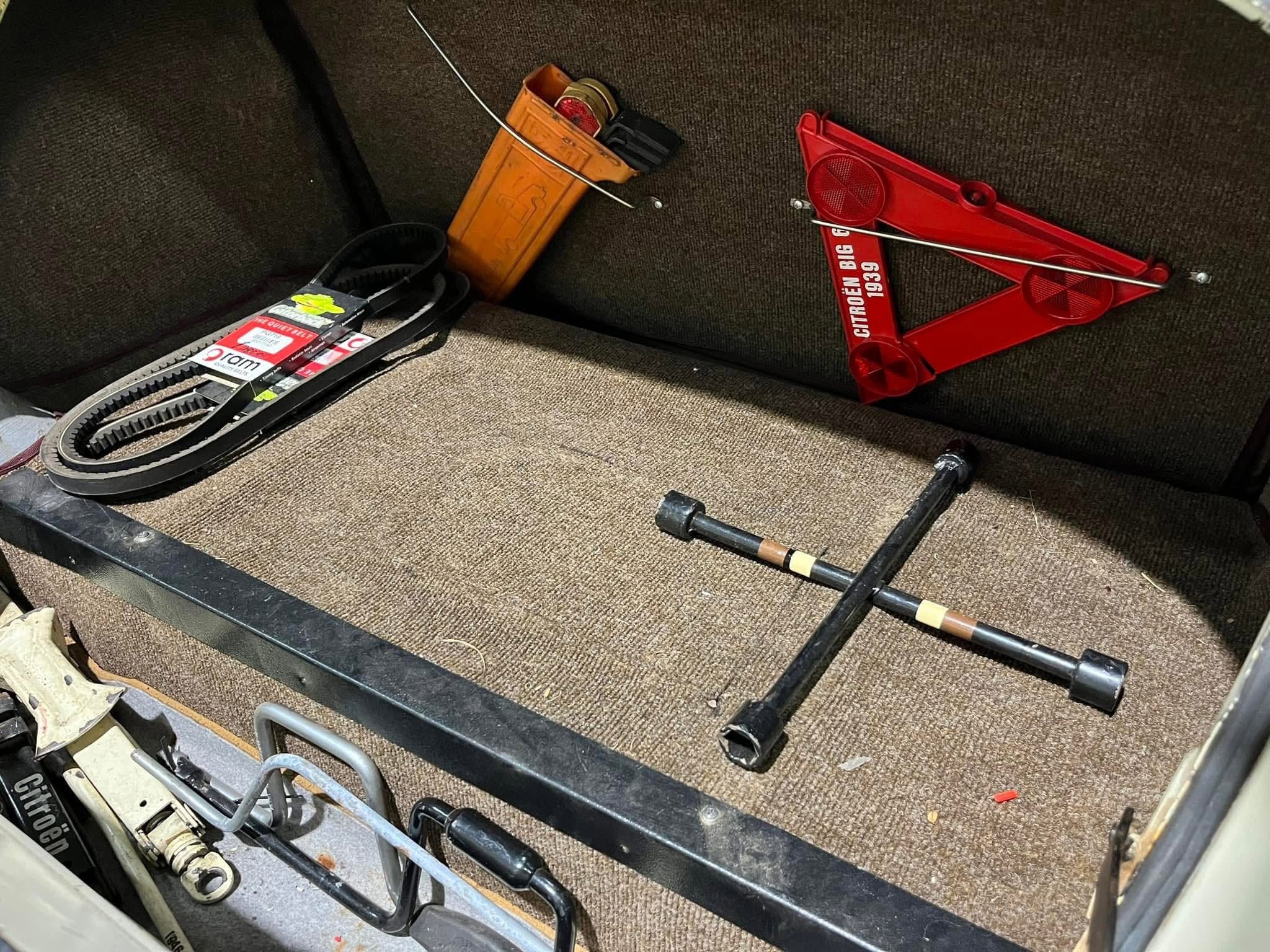 Red portable car jack and assorted repair tools scattered in a car trunk on brown carpeted surface.] ,