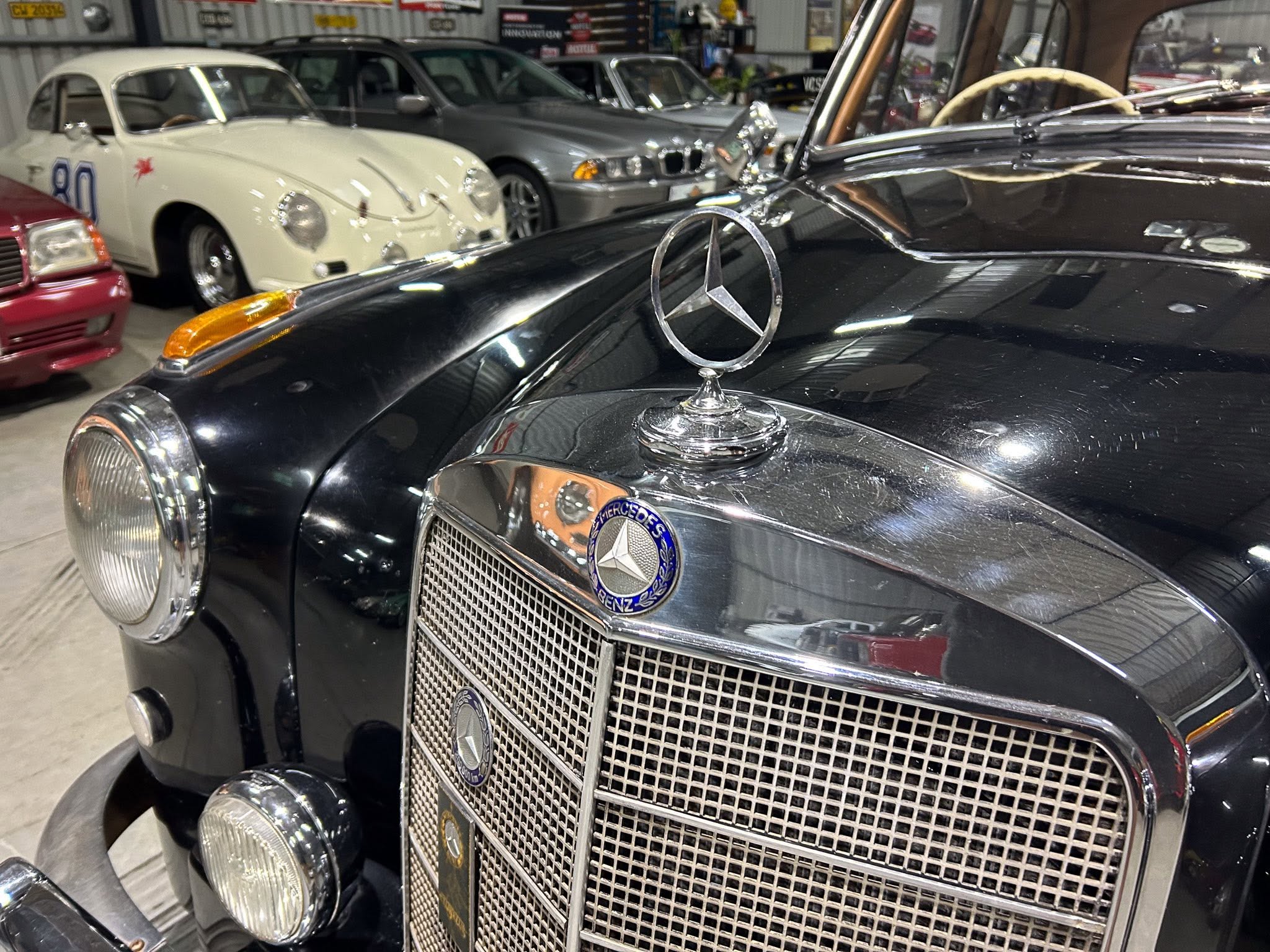 Front view of a black classic Mercedes-Benz with the iconic star hood ornament and large chrome grille in a showroom filled with other vintage cars