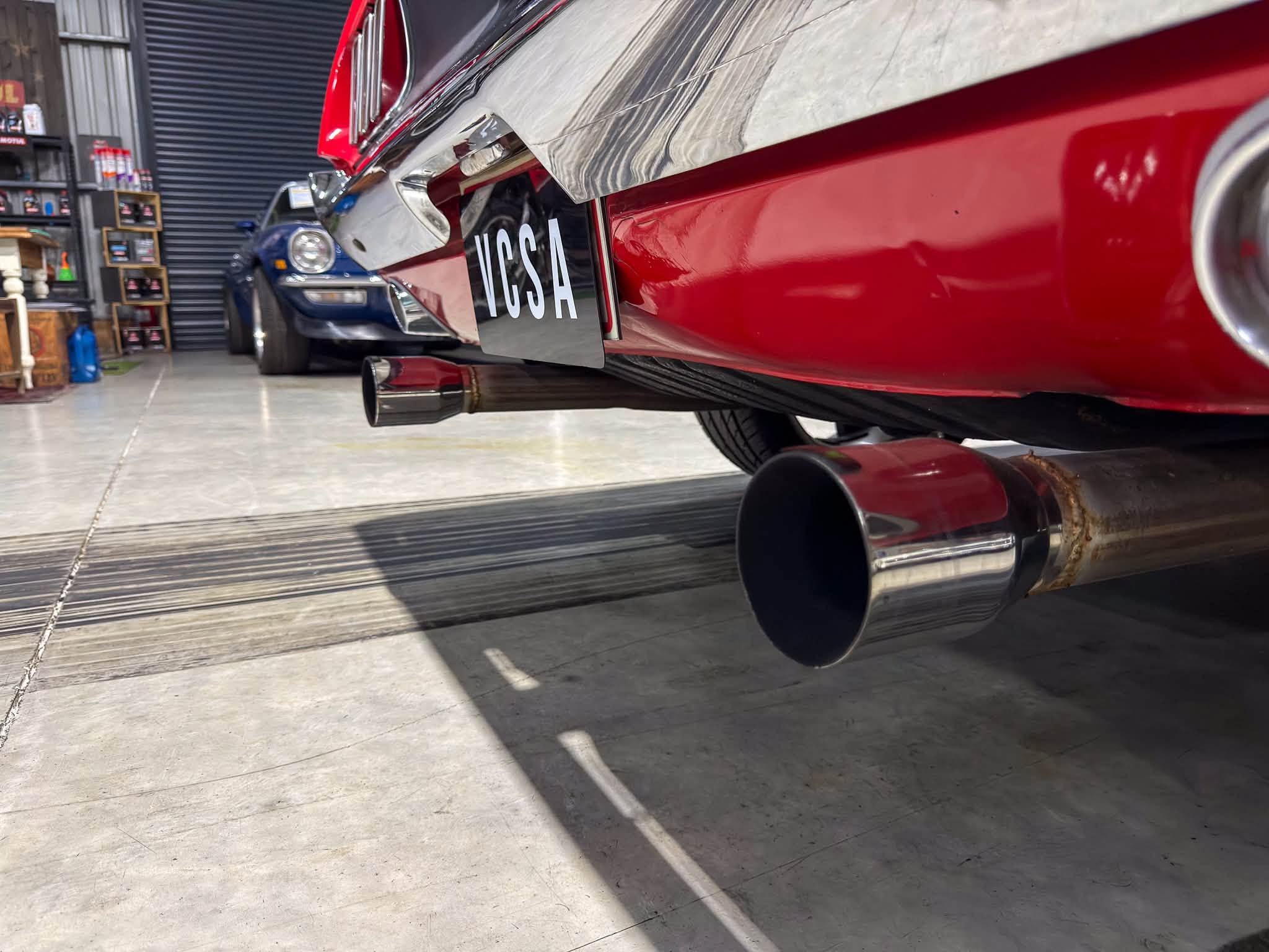 Close-up of the rear underside of a red car on a lift in a workshop, exposing the chrome exhaust and 'USA' license plate.