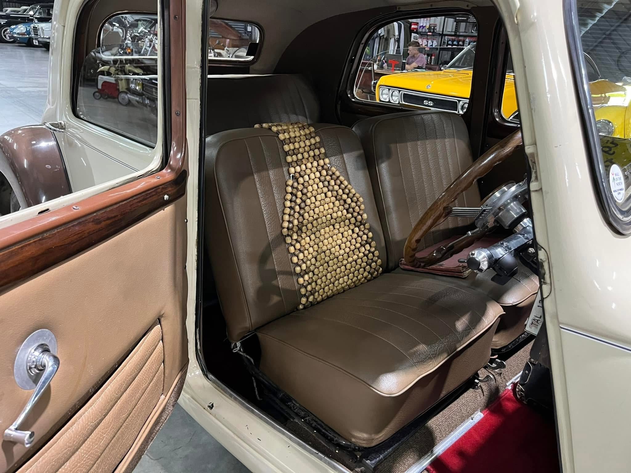 Interior of a vintage car with brown leather seats and a wooden steering wheel; beaded seat cover draped over the front seat.