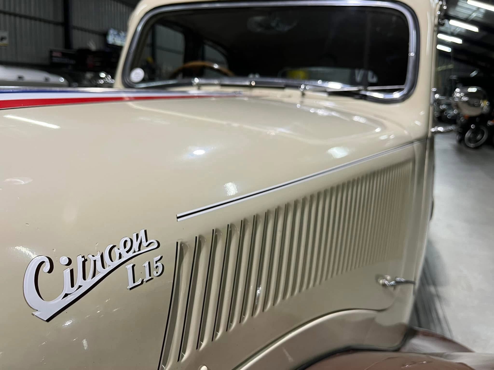 Close-up of a beige vintage car’s front fender with a red pinstripe and chrome trim; part of a cursive badge is visible on the door.