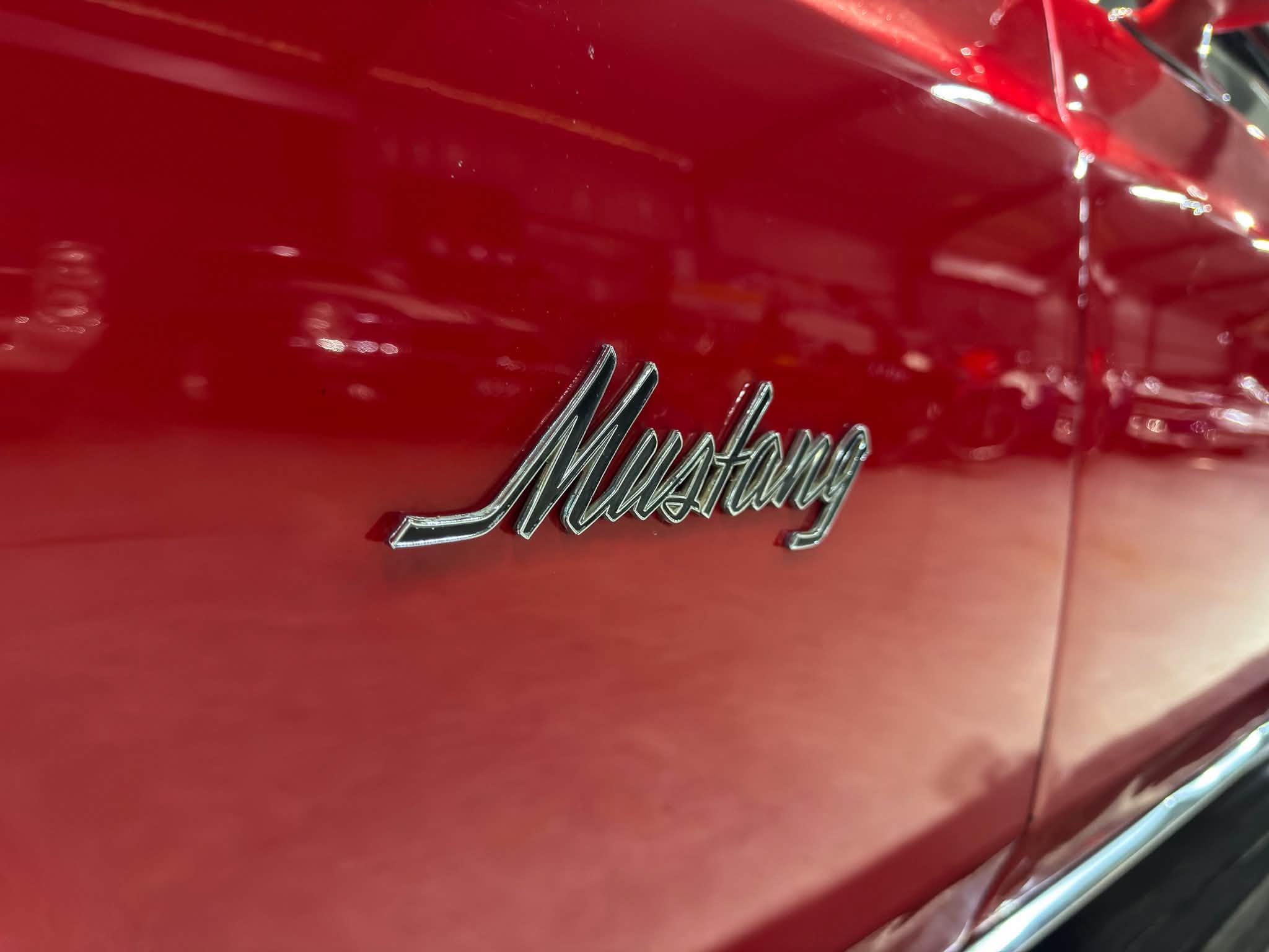 Close-up of a red car body featuring a chrome 'Mustang' script badge along the side.