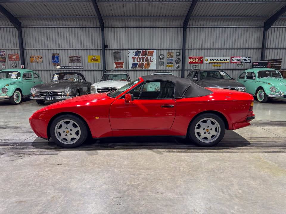 Profile view of a bright red two‑door convertible with a black soft top in a vintage car showroom.