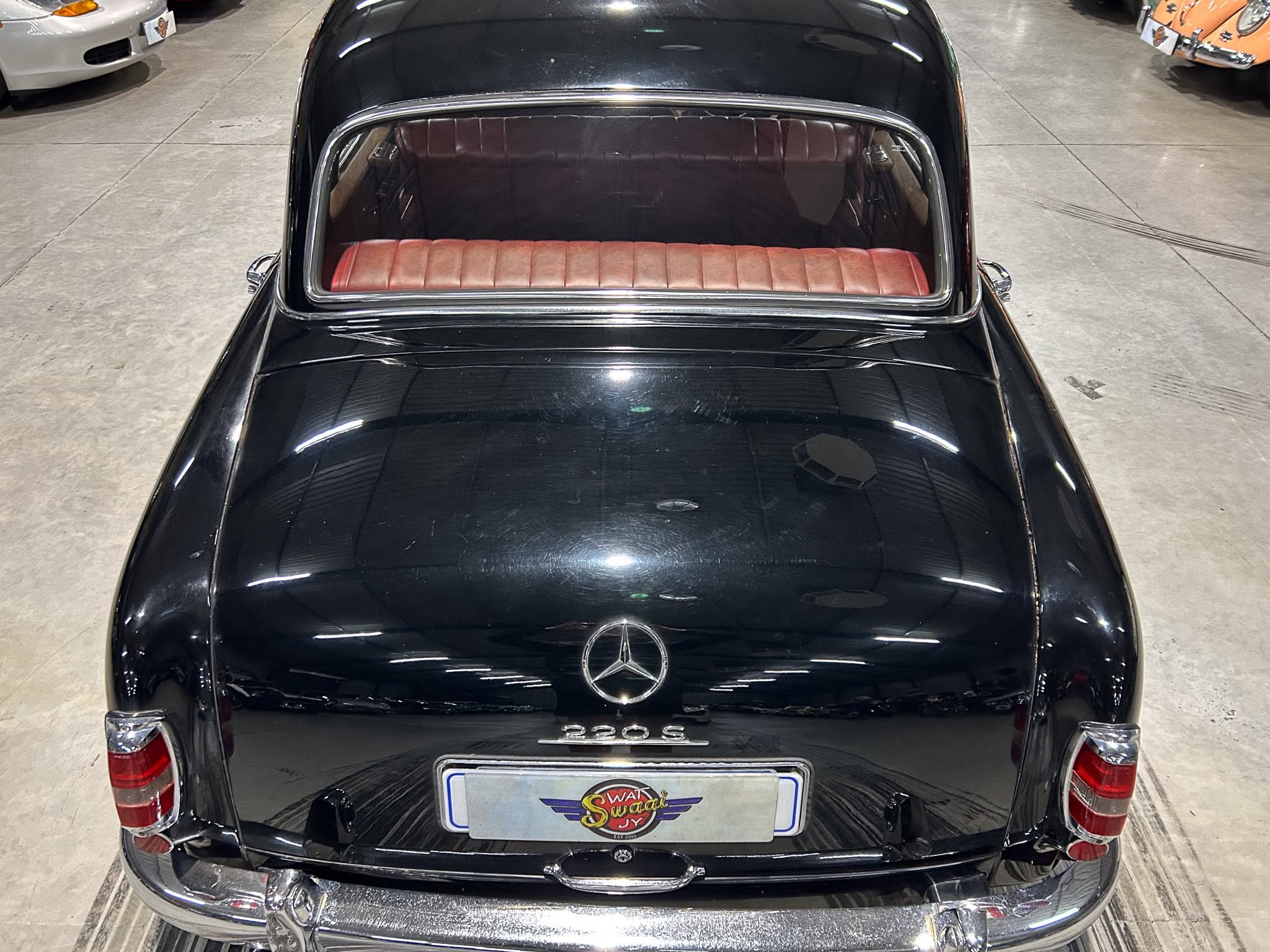 Rear view of a glossy black classic Mercedes-Benz 220S with red leather rear seat, photographed in a showroom showroom setting.